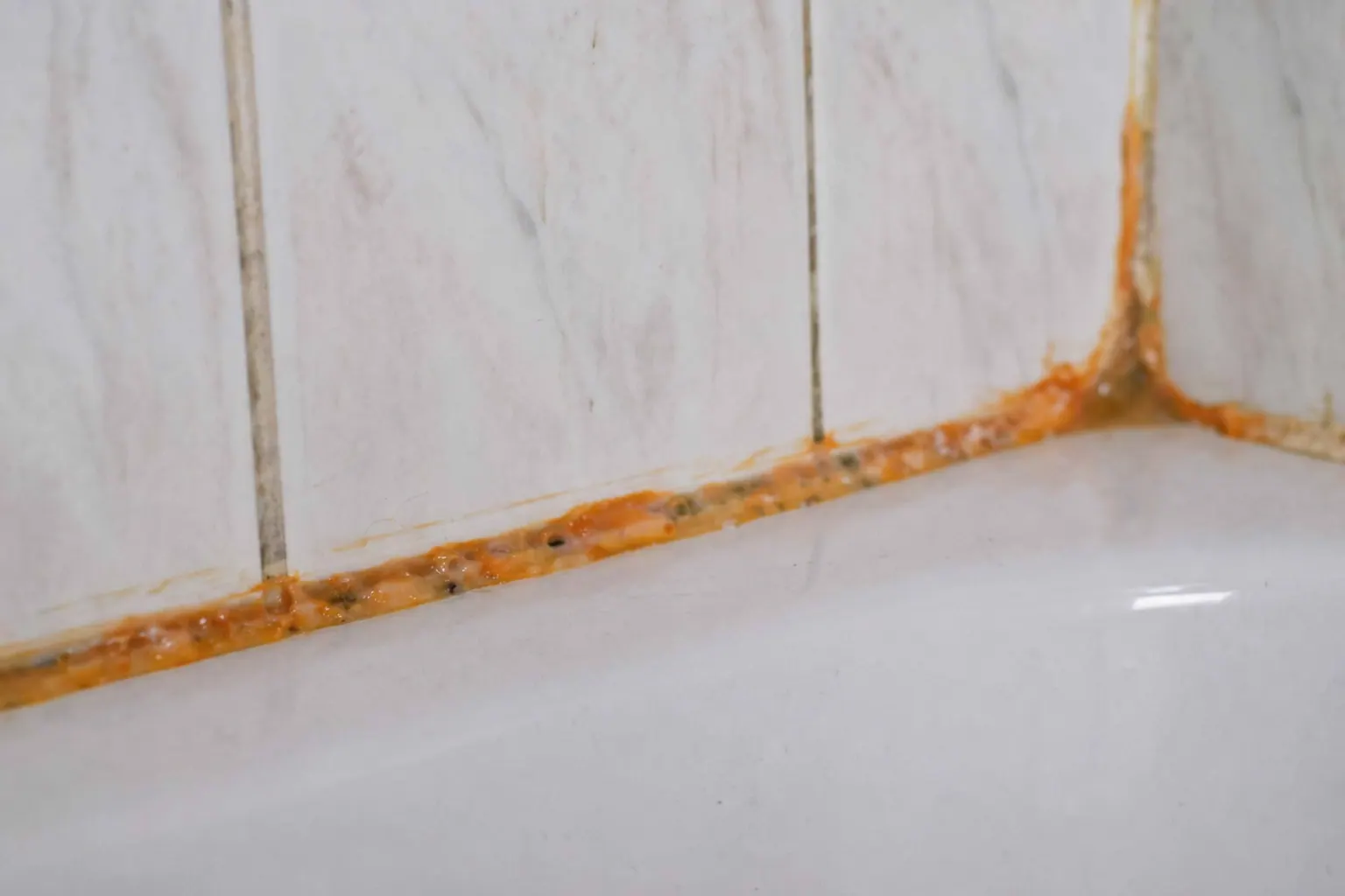 Orangefarbener, schleimiger Belag auf den Silikonfugen eines Altbau-Badezimmers ohne Fenster, Nahaufnahme
